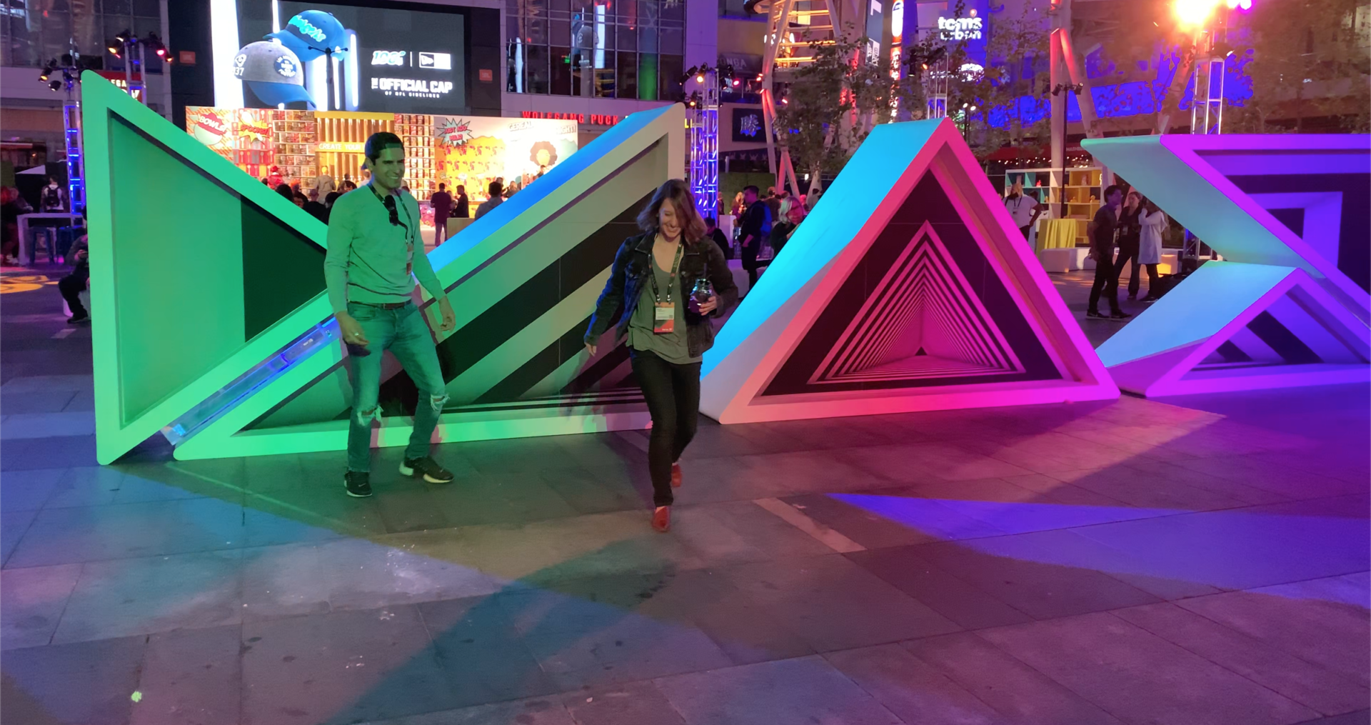 Two people walking under green, blue and purple lights